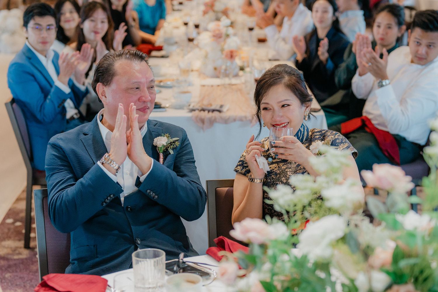 Couple sharing an emotional moment at wedding reception table decorated with floral centerpieces.