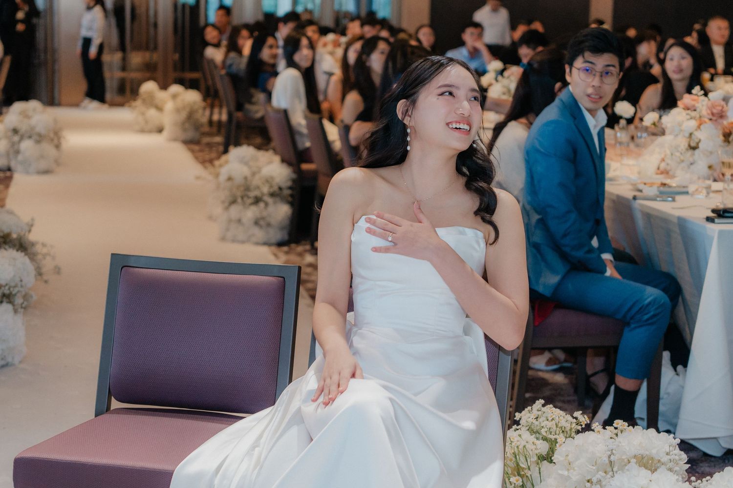 A bride in white gown sits gracefully during an elegant wedding reception.