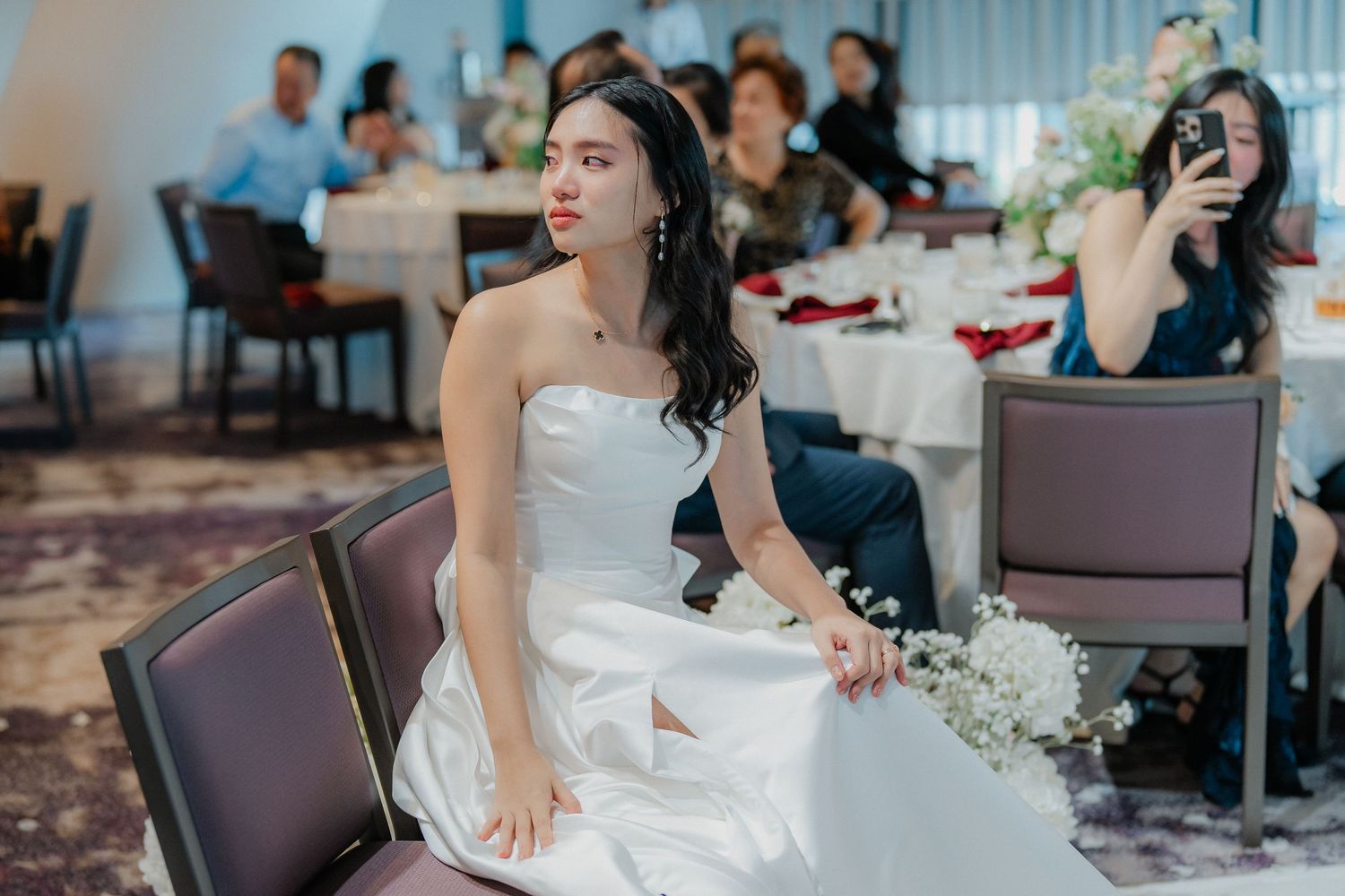 Reception guests gathered at decorated tables with white tablecloths in an elegant wedding venue.