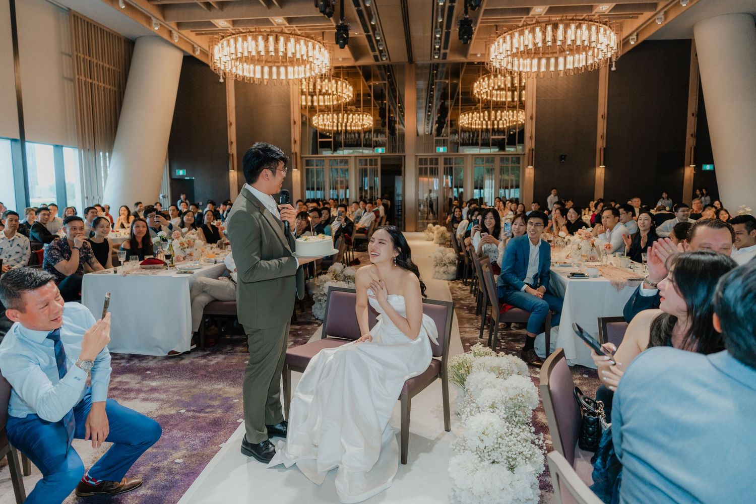 Elegant wedding venue with crystal chandeliers and guests seated at round tables for the reception.
