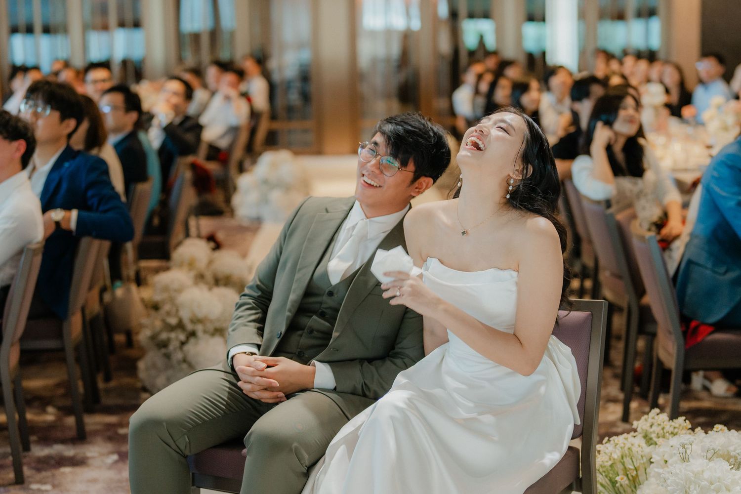 Wedding guests gather in an elegant ballroom with wooden paneled walls and modern lighting.