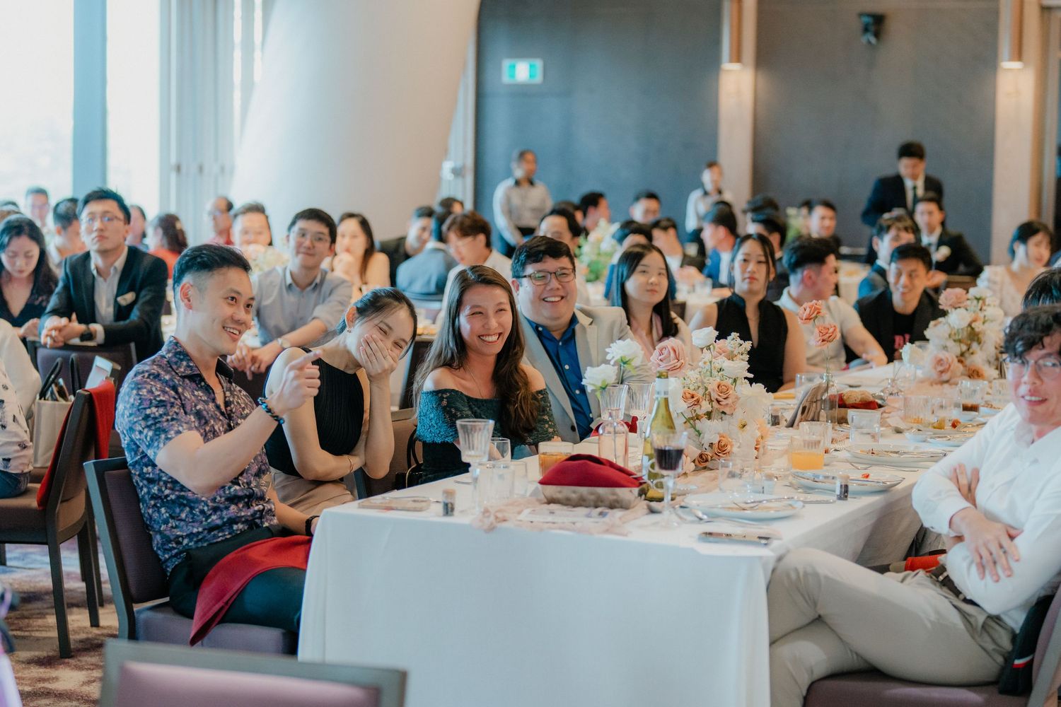 A banquet hall filled with wedding guests seated at decorated round tables during a reception.