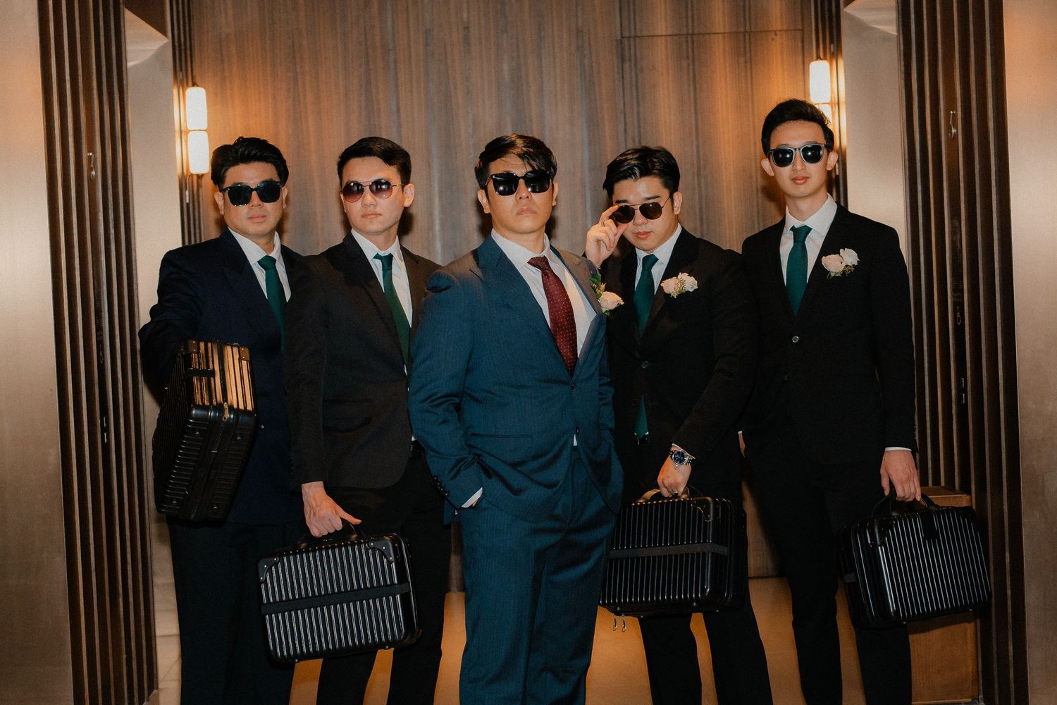 Stylish groomsmen in dark suits and sunglasses posing in modern hallway.