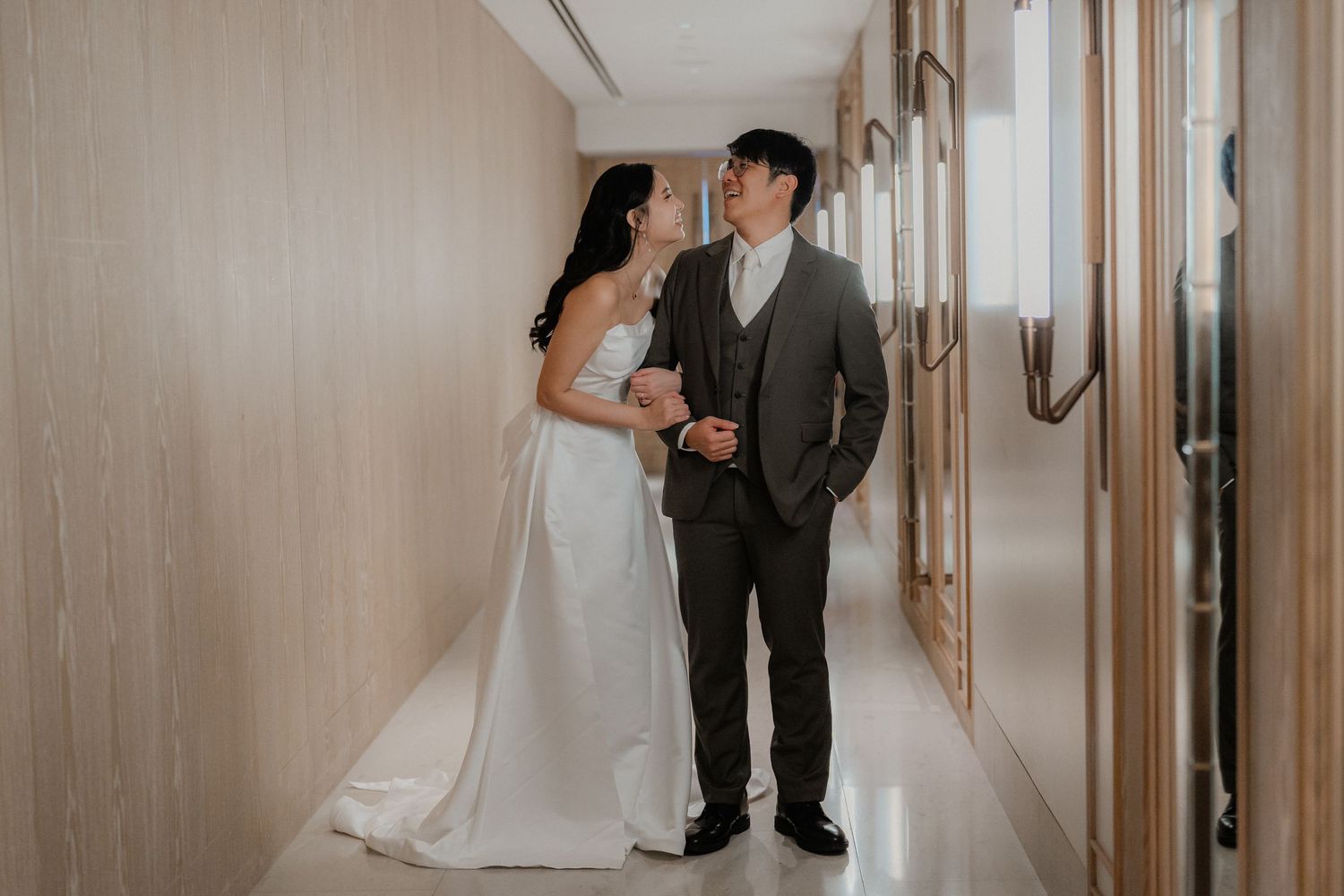 Couple in wedding attire sharing a private moment in a modern hotel hallway.