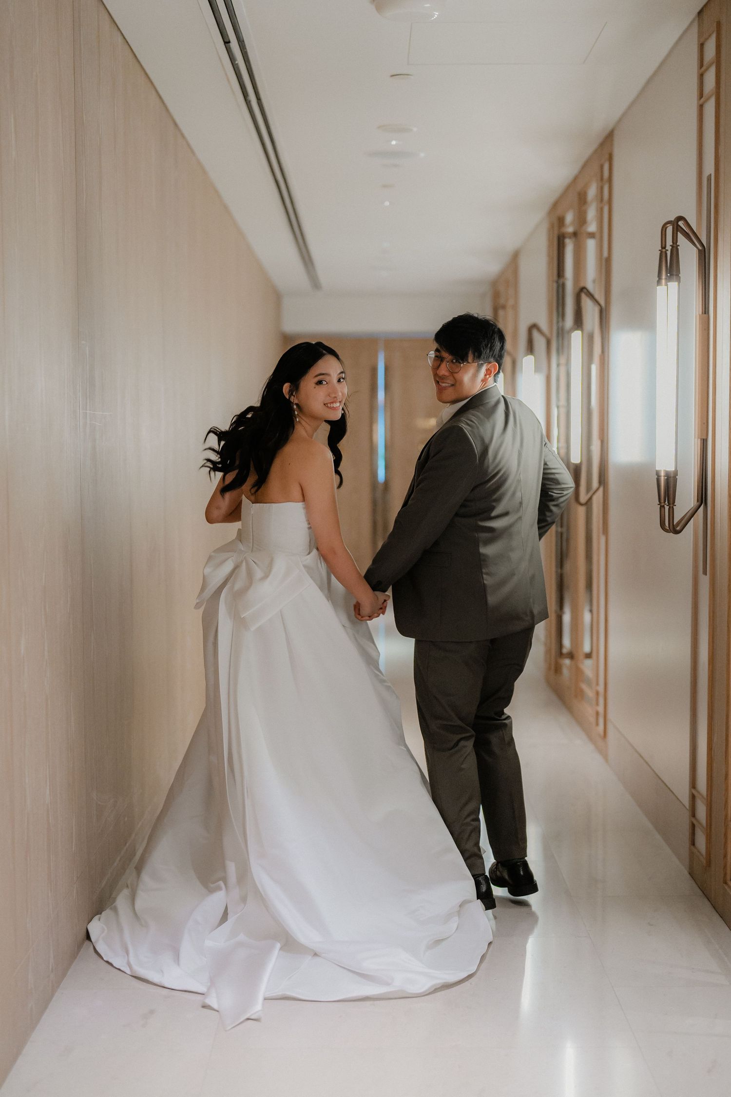 A wedding couple walking down an elegant hallway, with the bride's white gown trailing behind them.