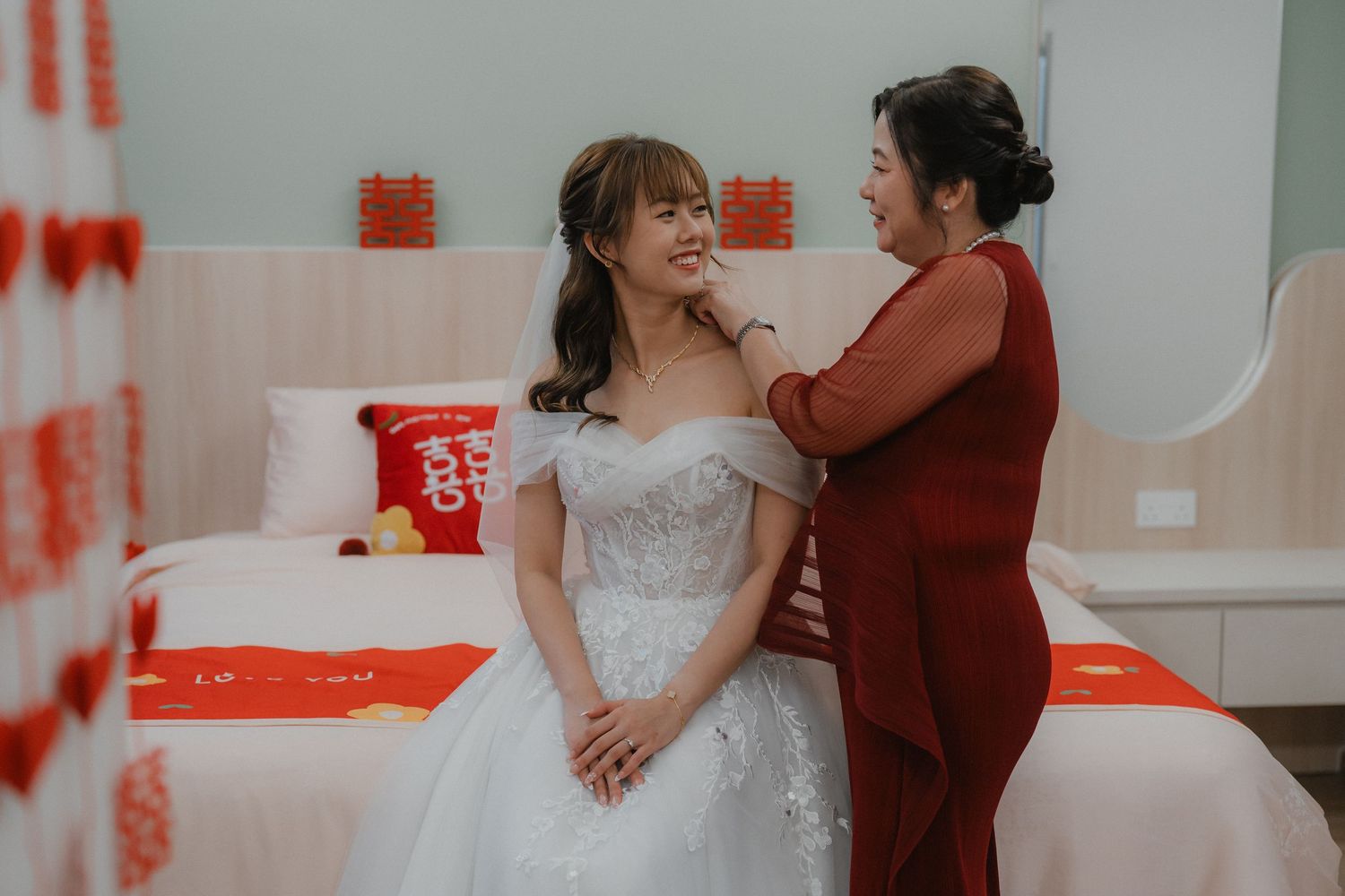 A tender moment during wedding preparations in a room with red decorative elements.
