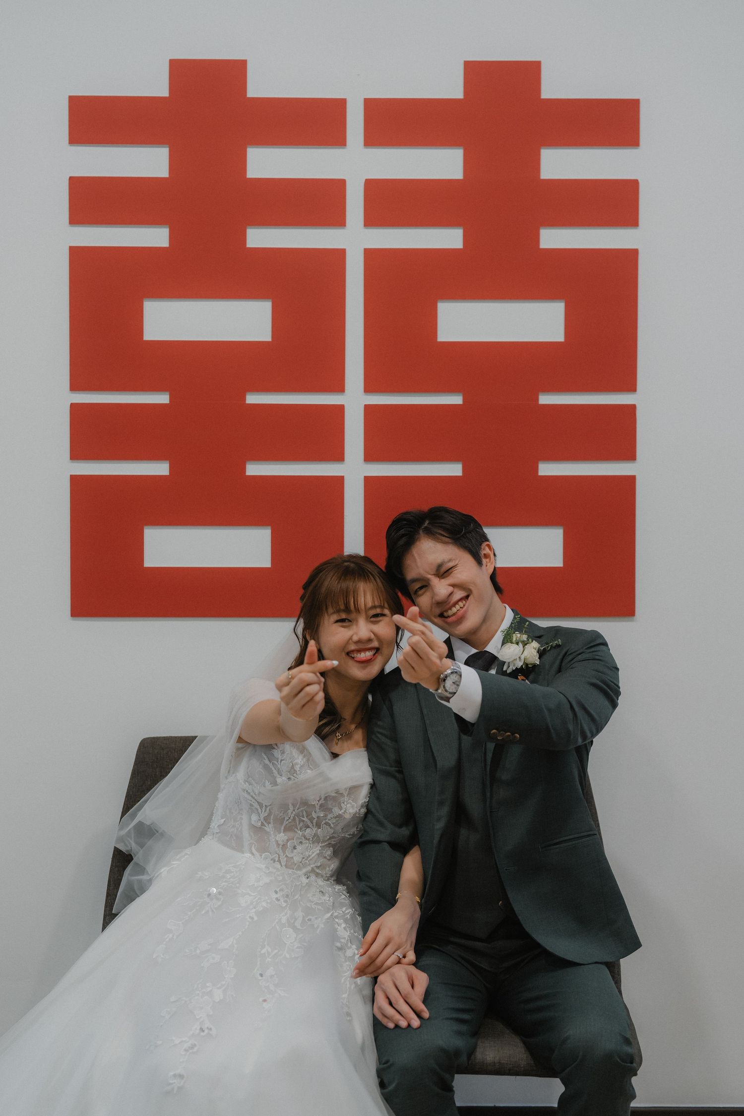 A romantic wedding couple poses against a wall with red Chinese double happiness characters.