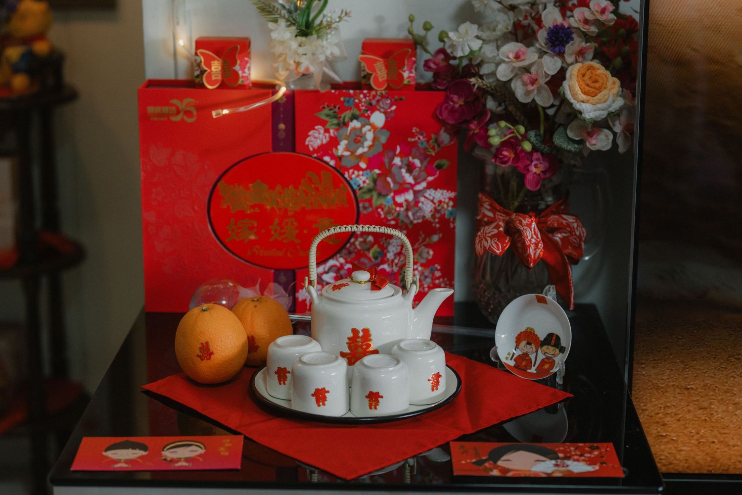 Traditional Chinese wedding decorations with red envelopes, teapot set and oranges on display.