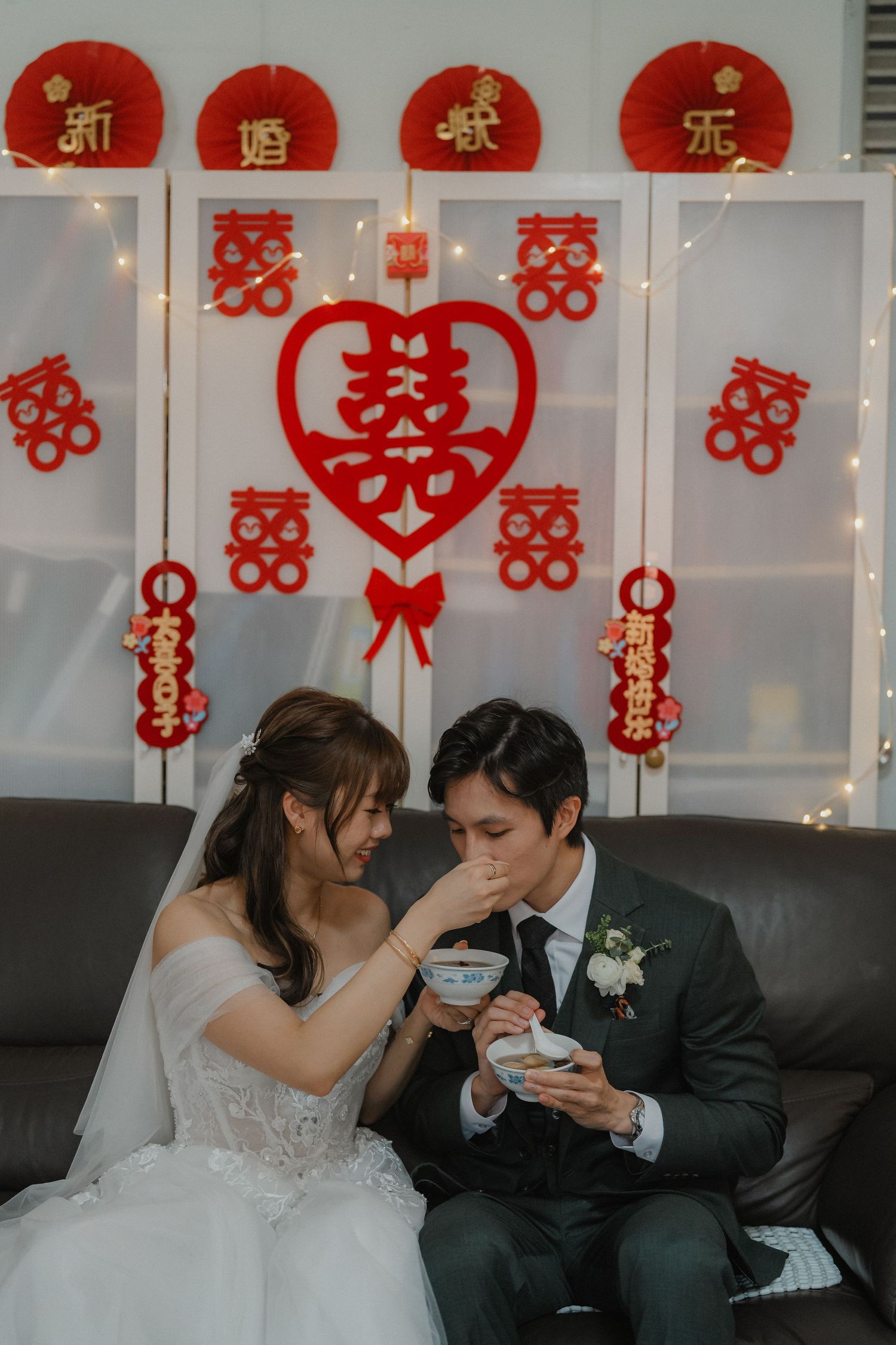 A couple enjoying boba tea together against traditional Chinese wedding decorations and double happiness symbols.