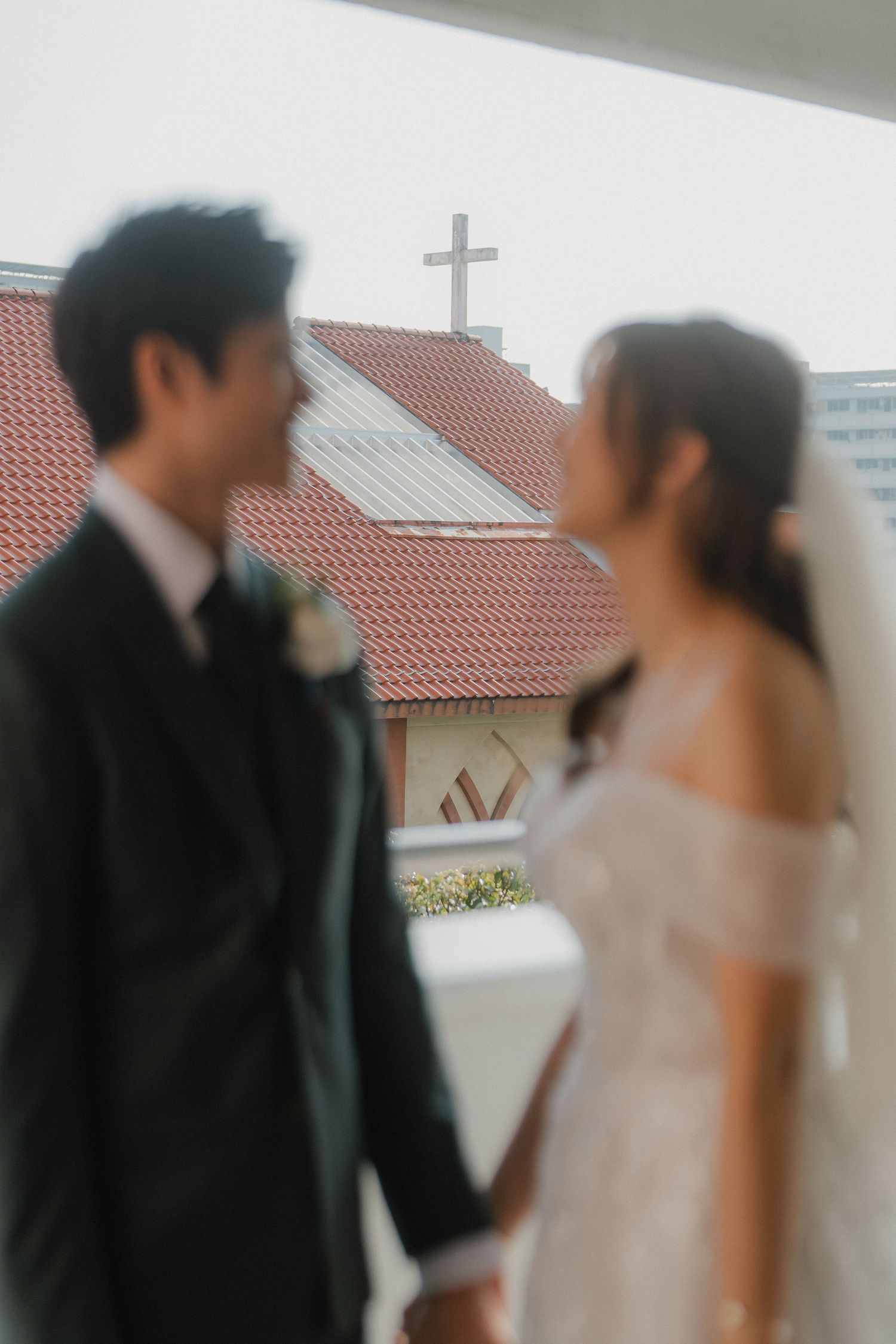 A romantic moment between a bride and groom in front of a building with red tile roof.