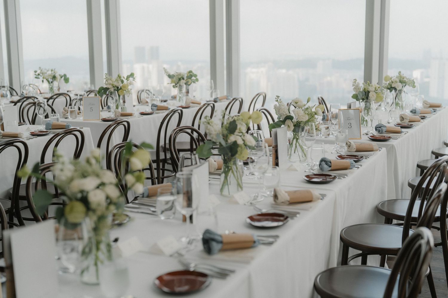 An elegant long banquet table set for a wedding reception with white linens and delicate floral centerpieces.