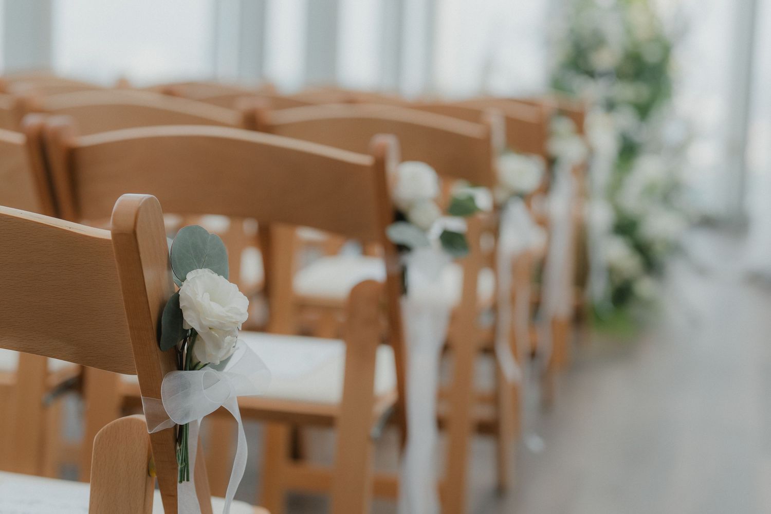 Wooden chairs lined up for an indoor wedding ceremony with soft fabric decorations.