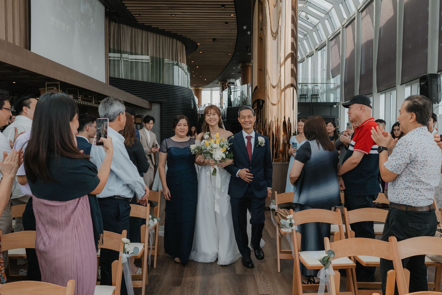 A wedding processional in a modern venue with natural light and wooden details.