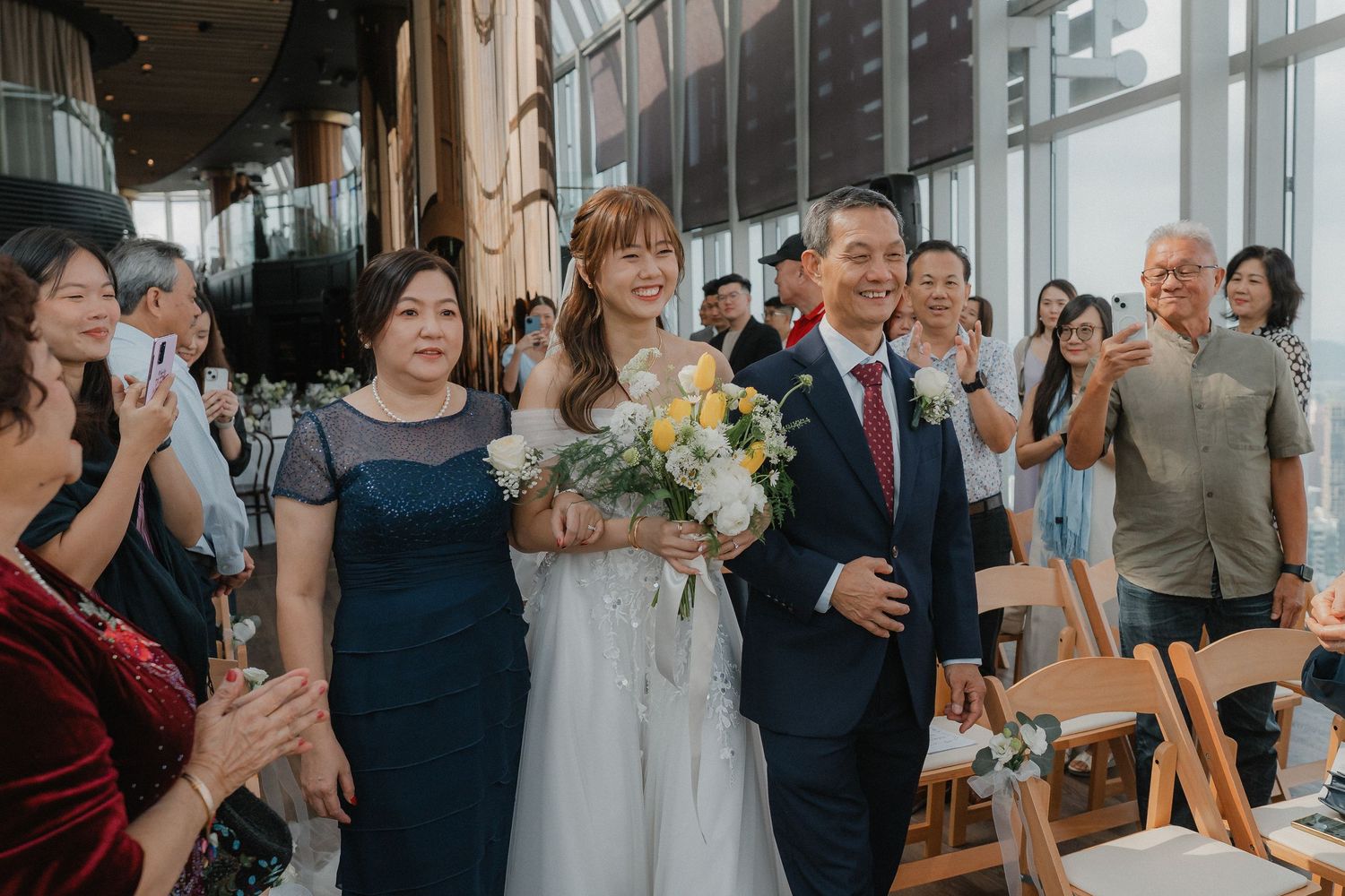 Wedding processional in modern venue with guests clapping along both sides of aisle.