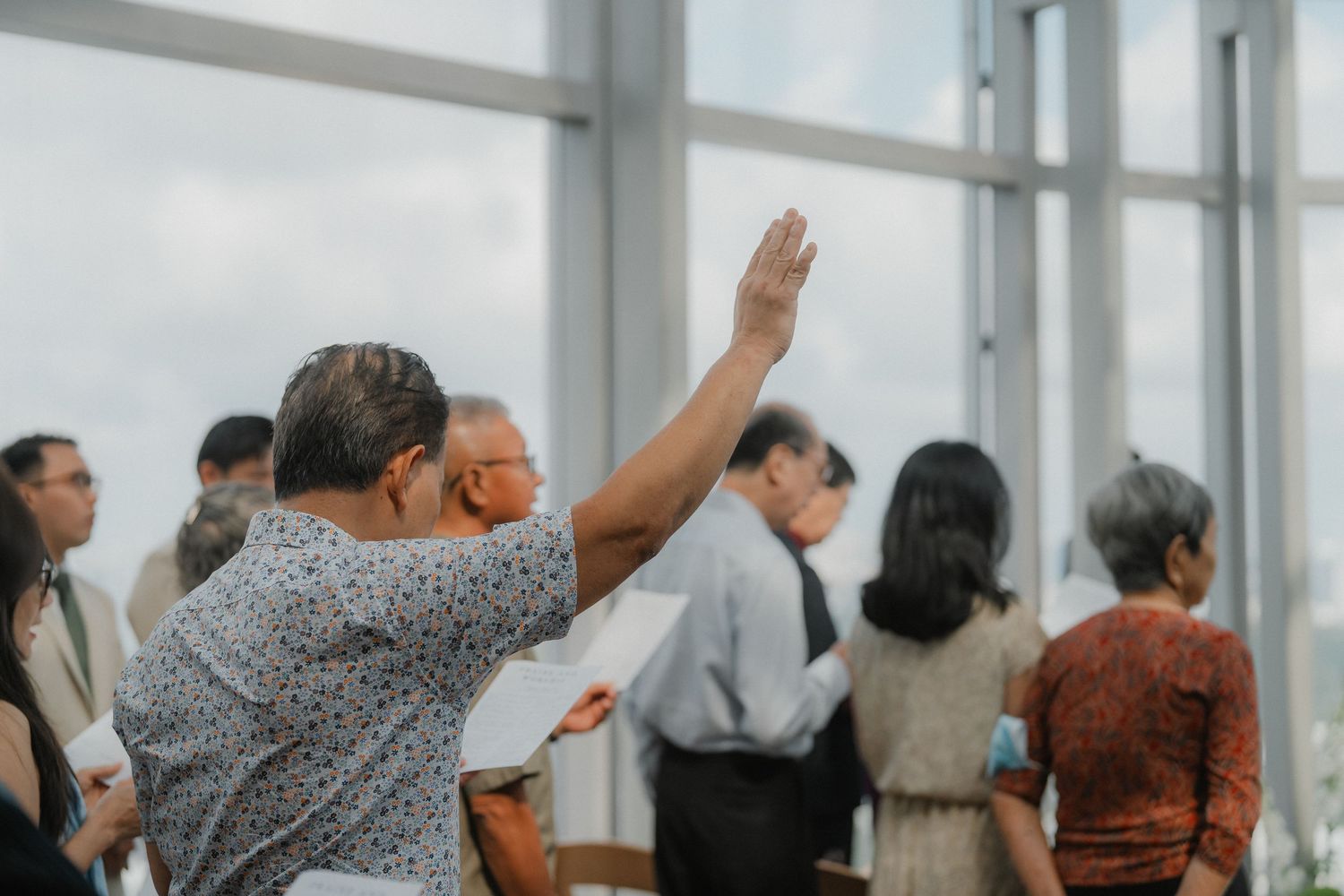 Wedding guests raise their hands during a celebration in a bright indoor venue.