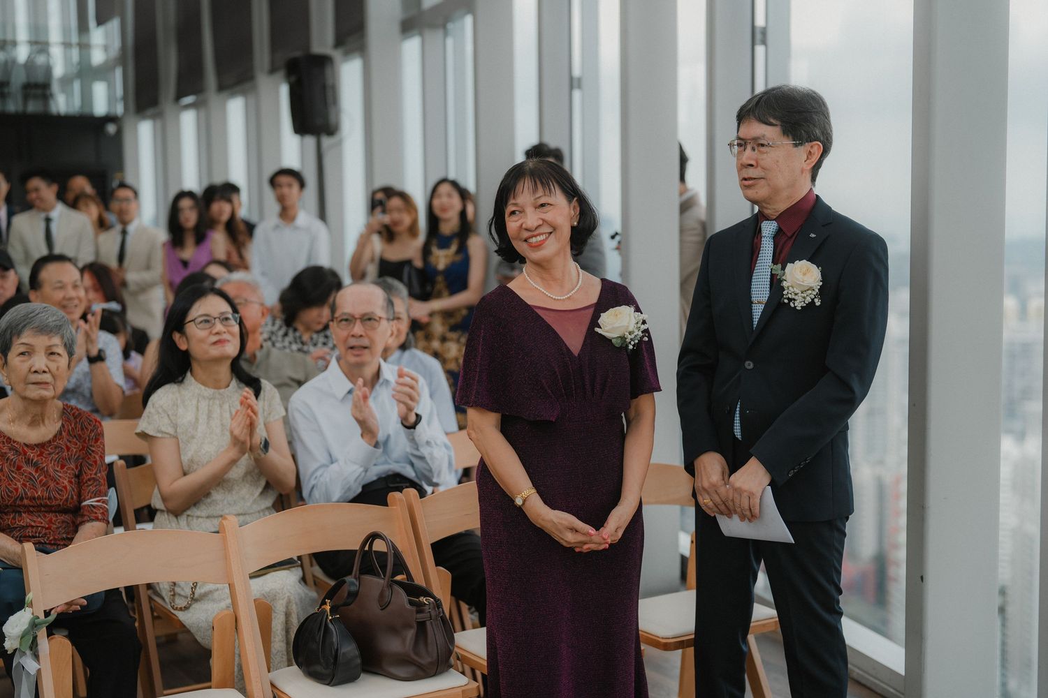 Wedding guests watching a ceremony in a modern venue with floor-to-ceiling windows.