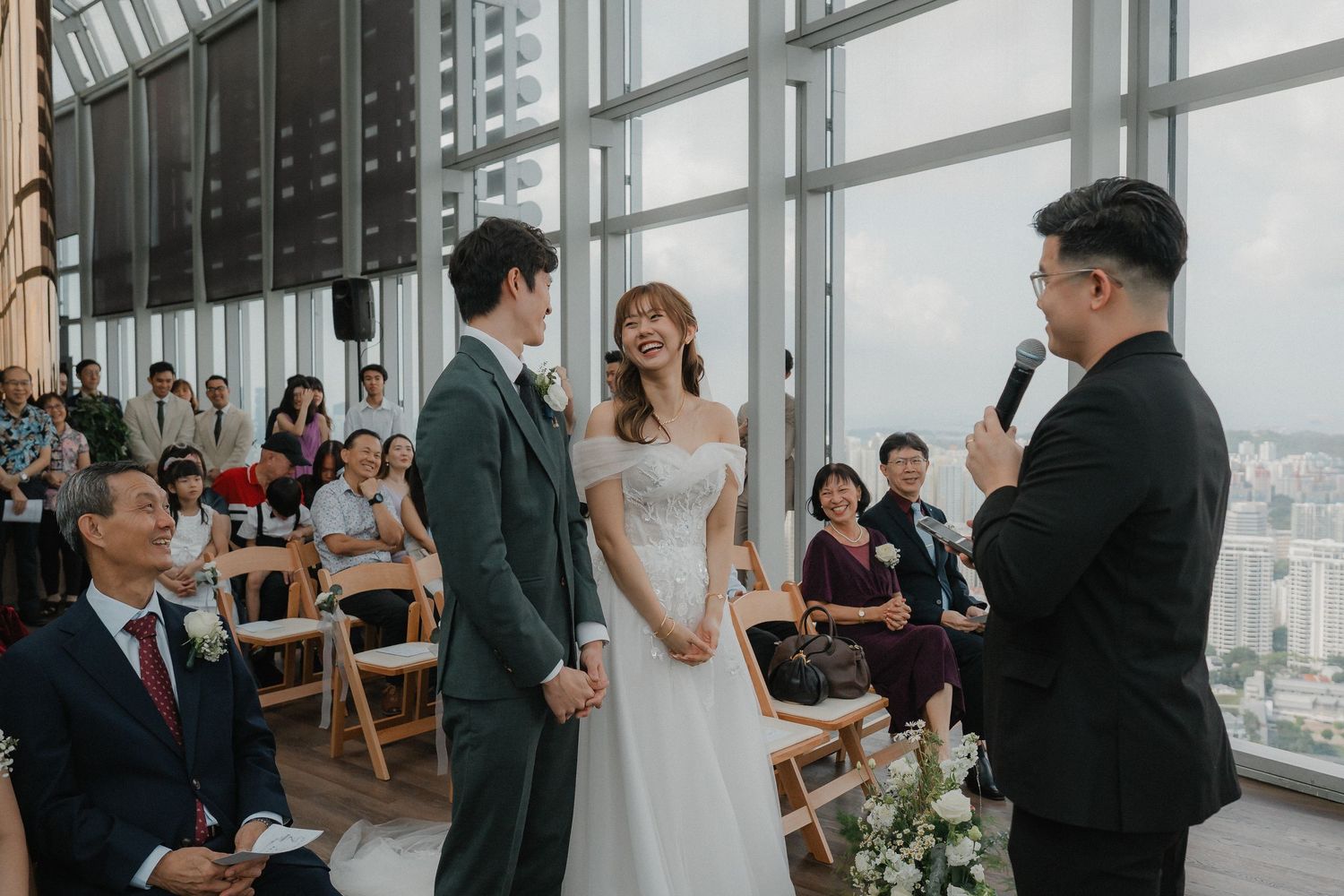 Wedding ceremony taking place in a modern venue with floor-to-ceiling windows overlooking a city skyline.