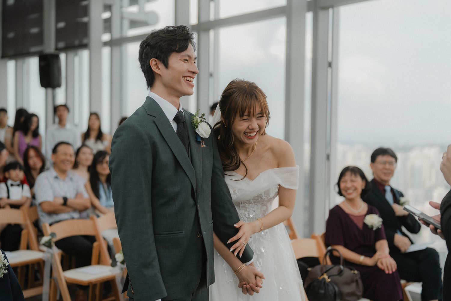 Elegant wedding ceremony taking place in modern venue with floor-to-ceiling windows.