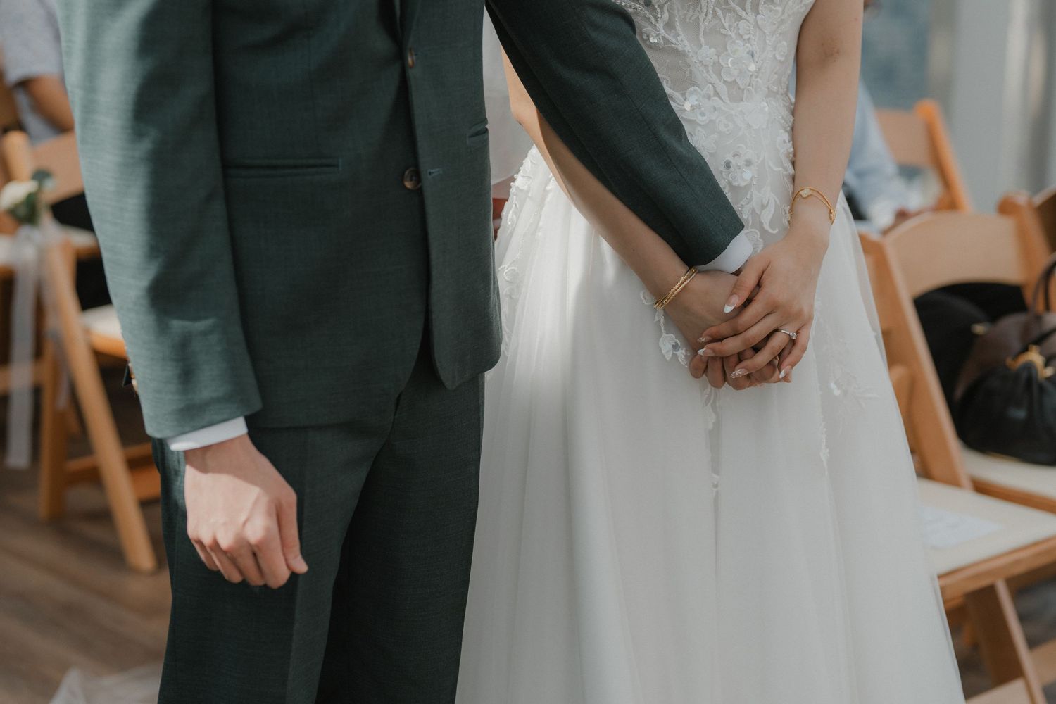 Close-up of couple holding hands during wedding ceremony, showing formal attire details.
