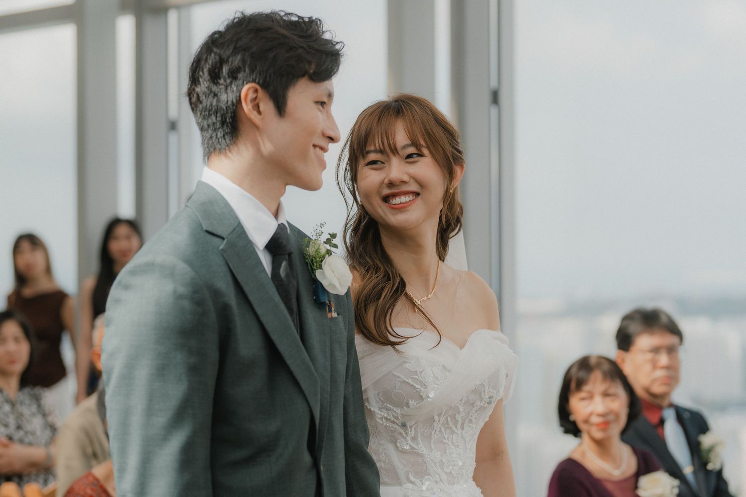 Wedding ceremony taking place in a bright modern venue with large windows and floral decorations.