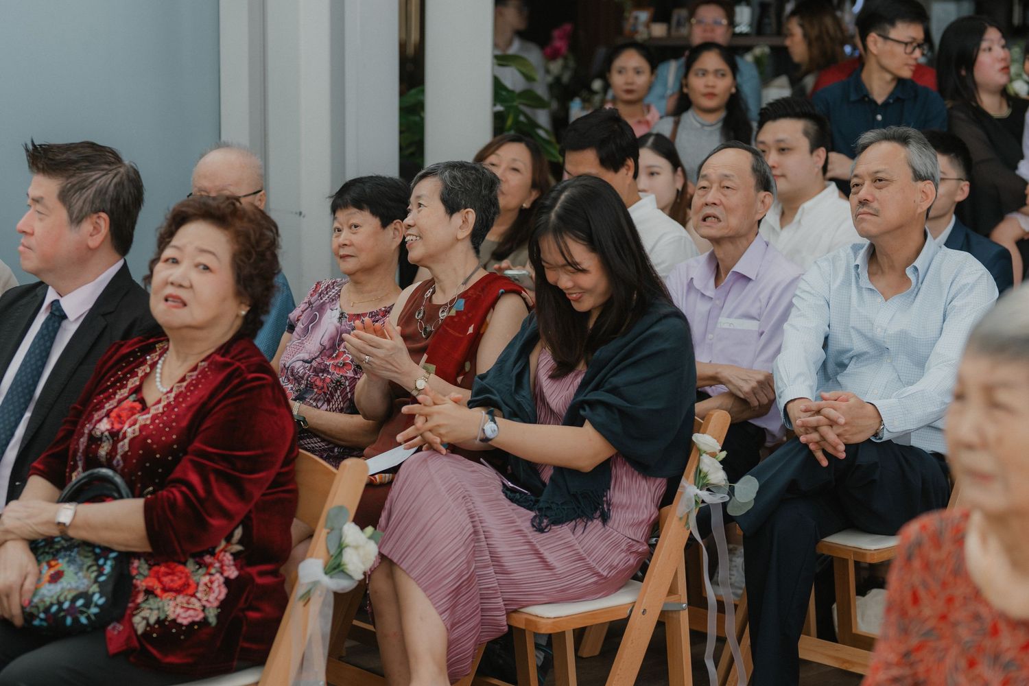 Wedding attendees react emotionally during ceremony in a bright, modern venue with glass walls.