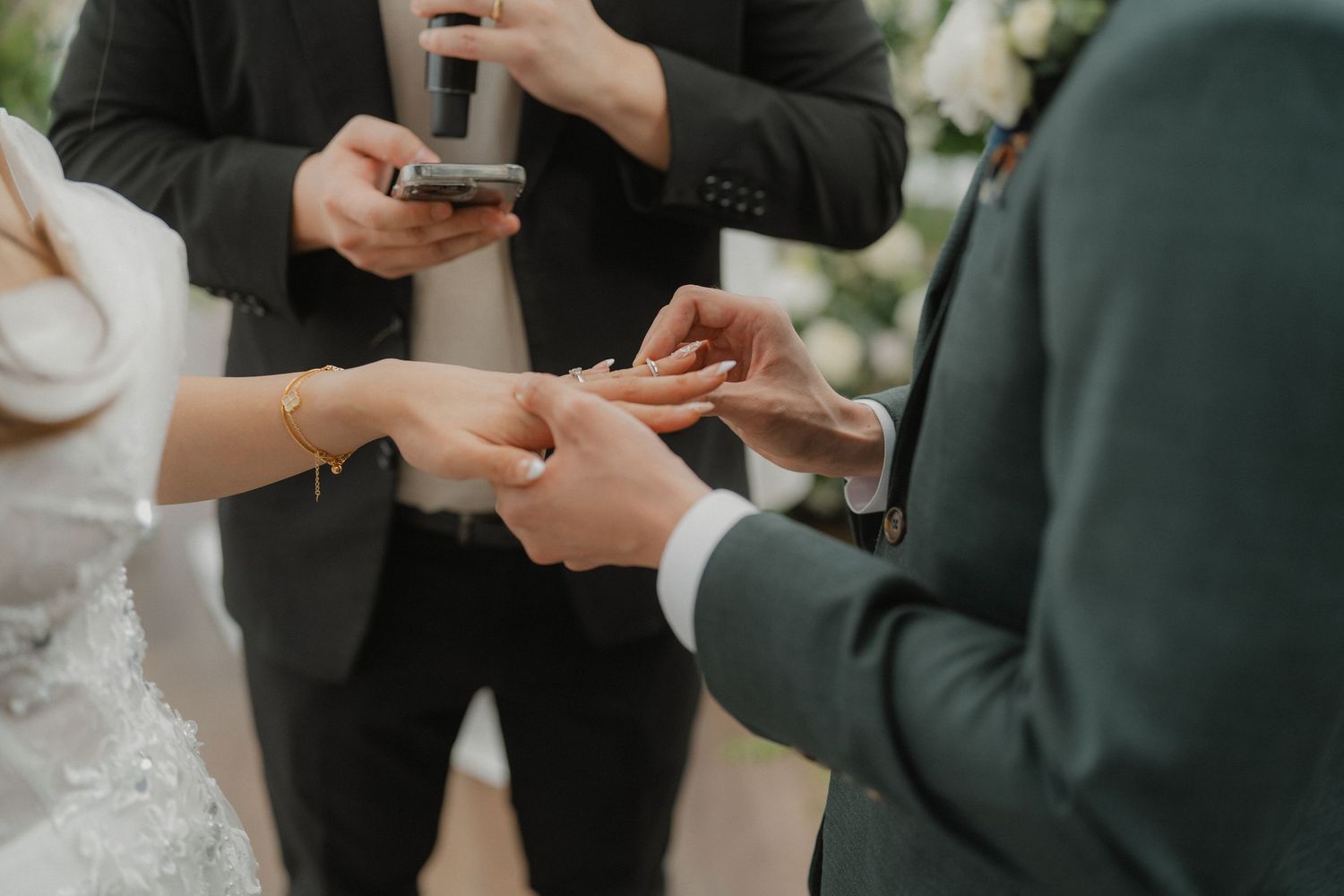 Close-up shot of wedding ring exchange during ceremony with hands in focus.