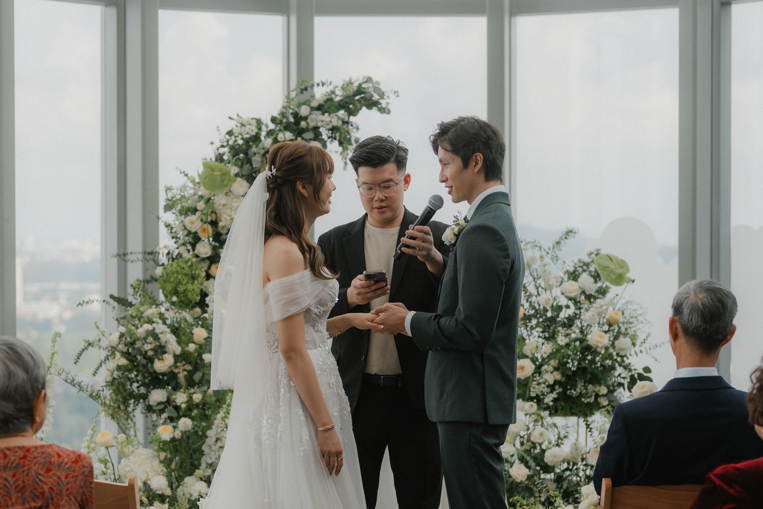 Wedding officiant conducts ceremony for couple under elegant floral decorations in modern venue.