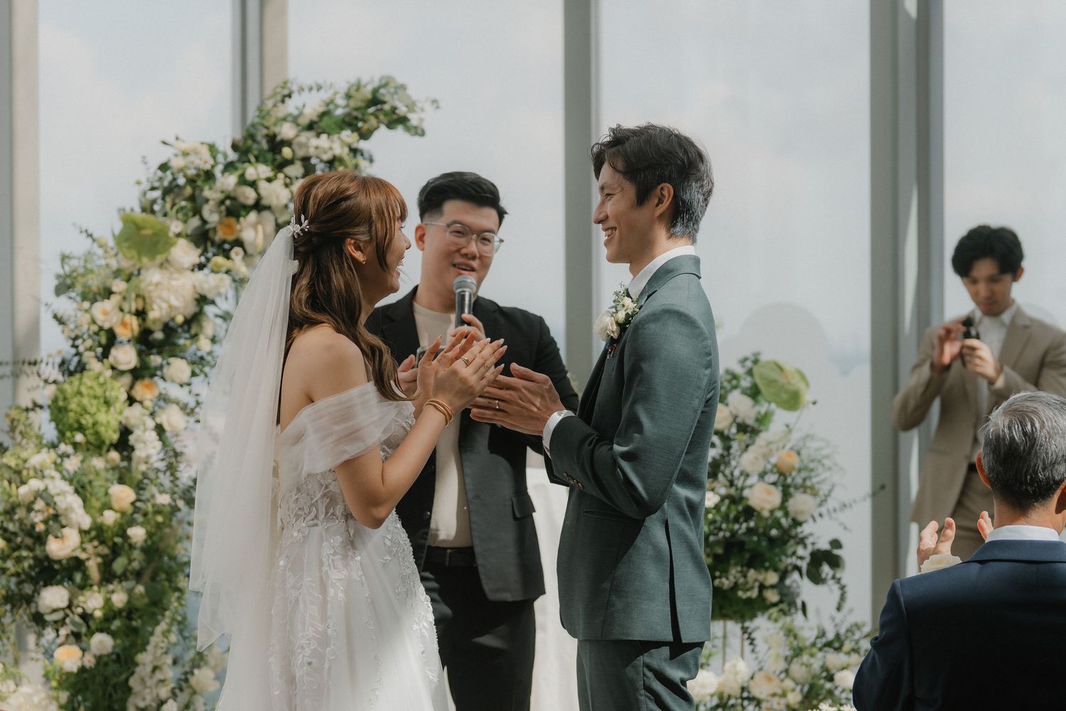 Wedding ceremony in progress under beautiful floral arch in modern venue with city views.