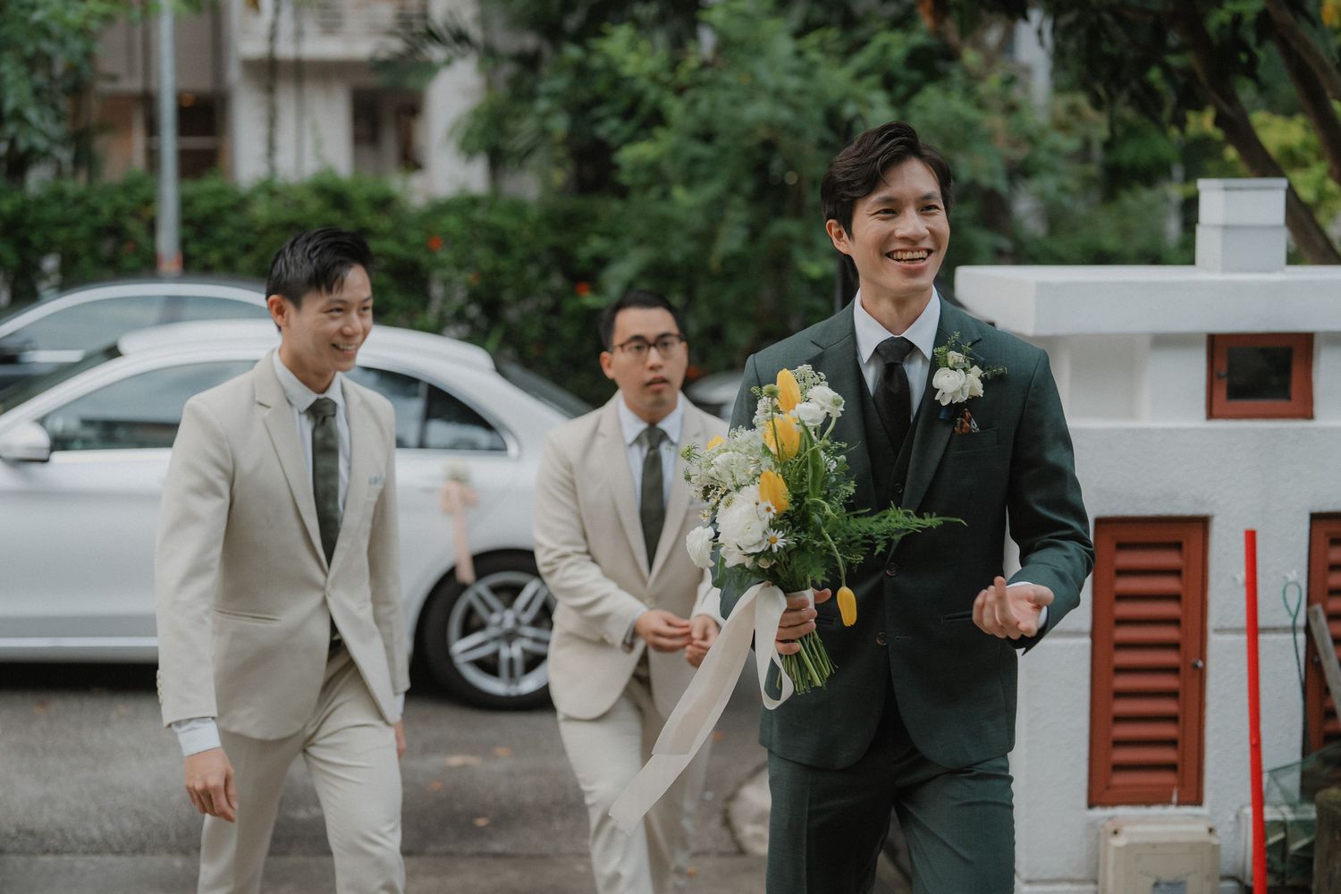 Three groomsmen walk together, with one carrying a floral bouquet.