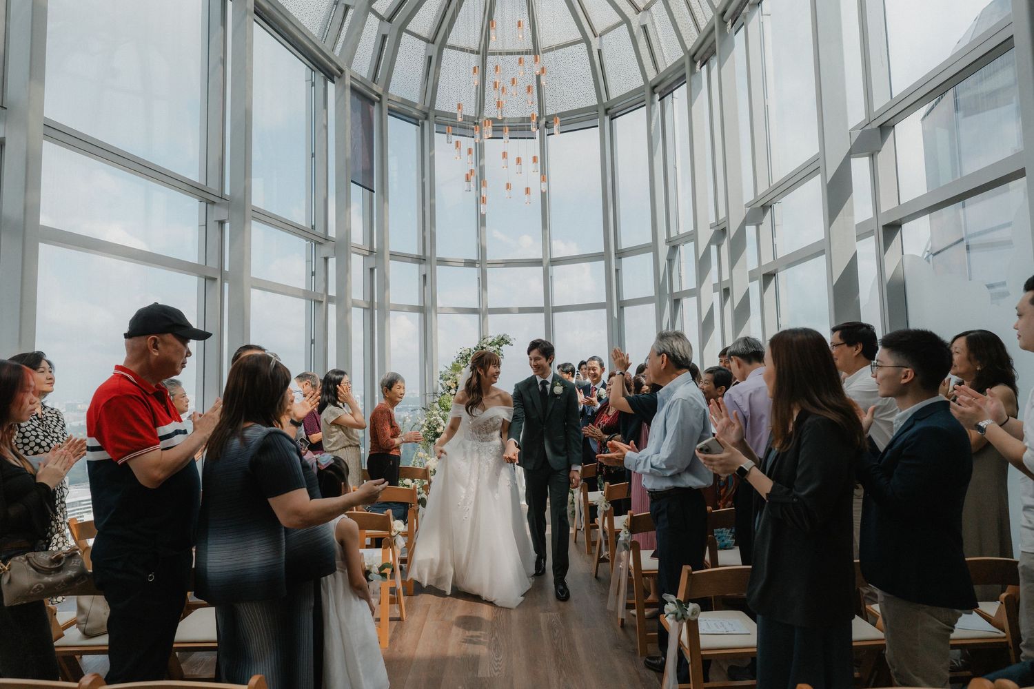 Wedding guests celebrating in a bright circular room with floor-to-ceiling windows and modern architecture.