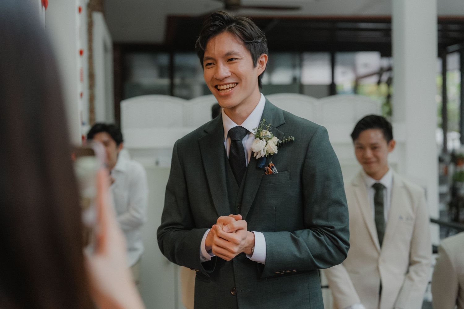 A groom in dark suit with boutonniere smiles during wedding ceremony.