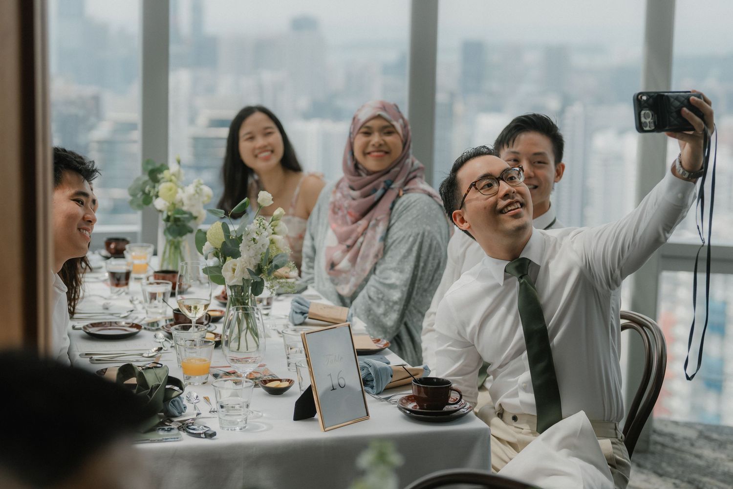 A group of people enjoying a meal together at a long dining table with city views in the background.