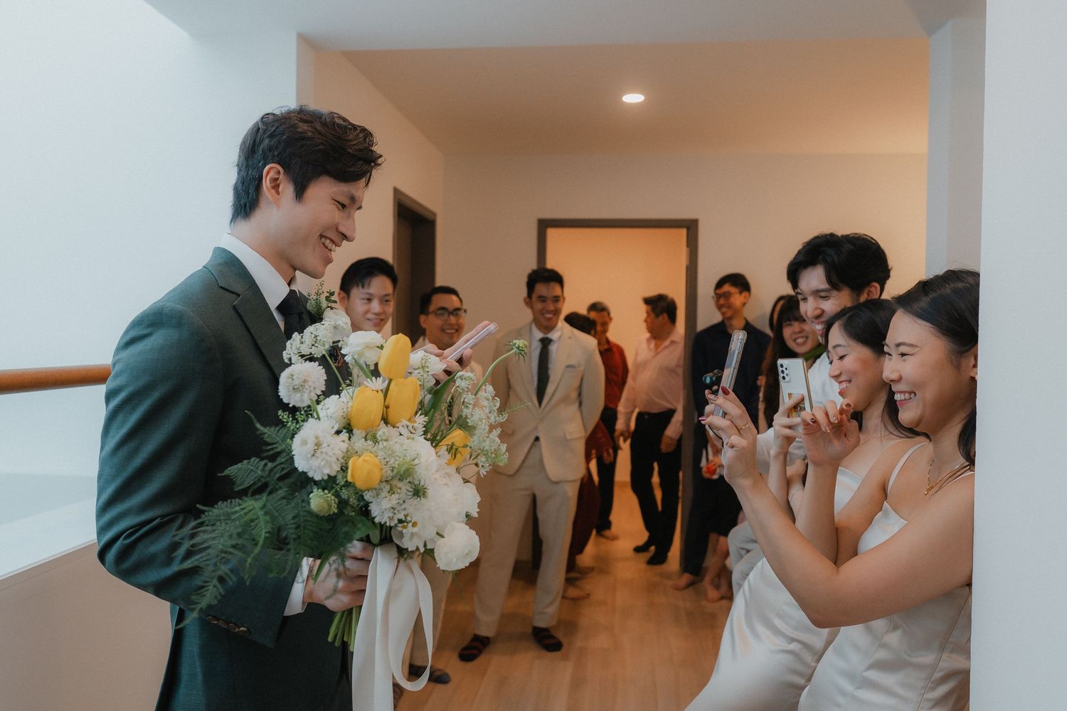 A groom holds a beautiful bouquet of white and yellow flowers during an indoor wedding ceremony.