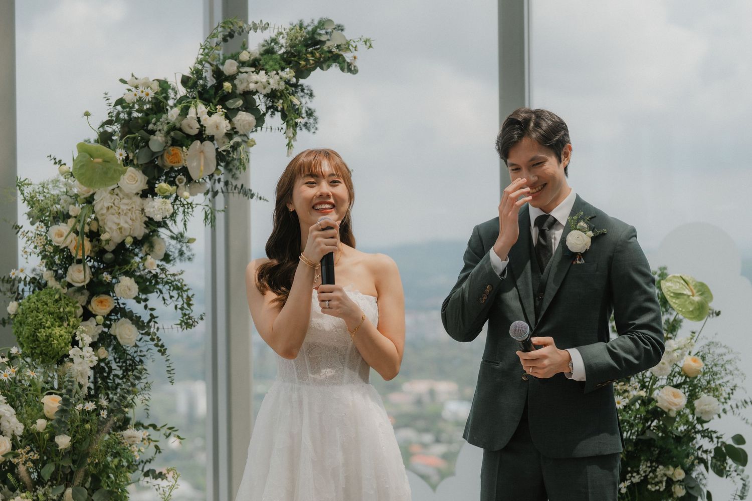 Wedding ceremony moment with floral arch and city views through large windows.