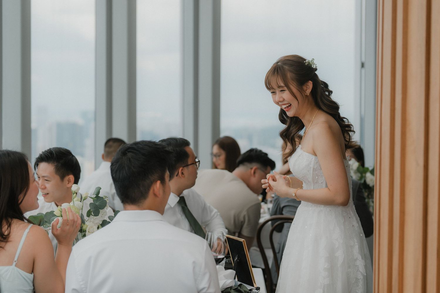 A bride in a white wedding dress stands at a reception table during an elegant indoor celebration.