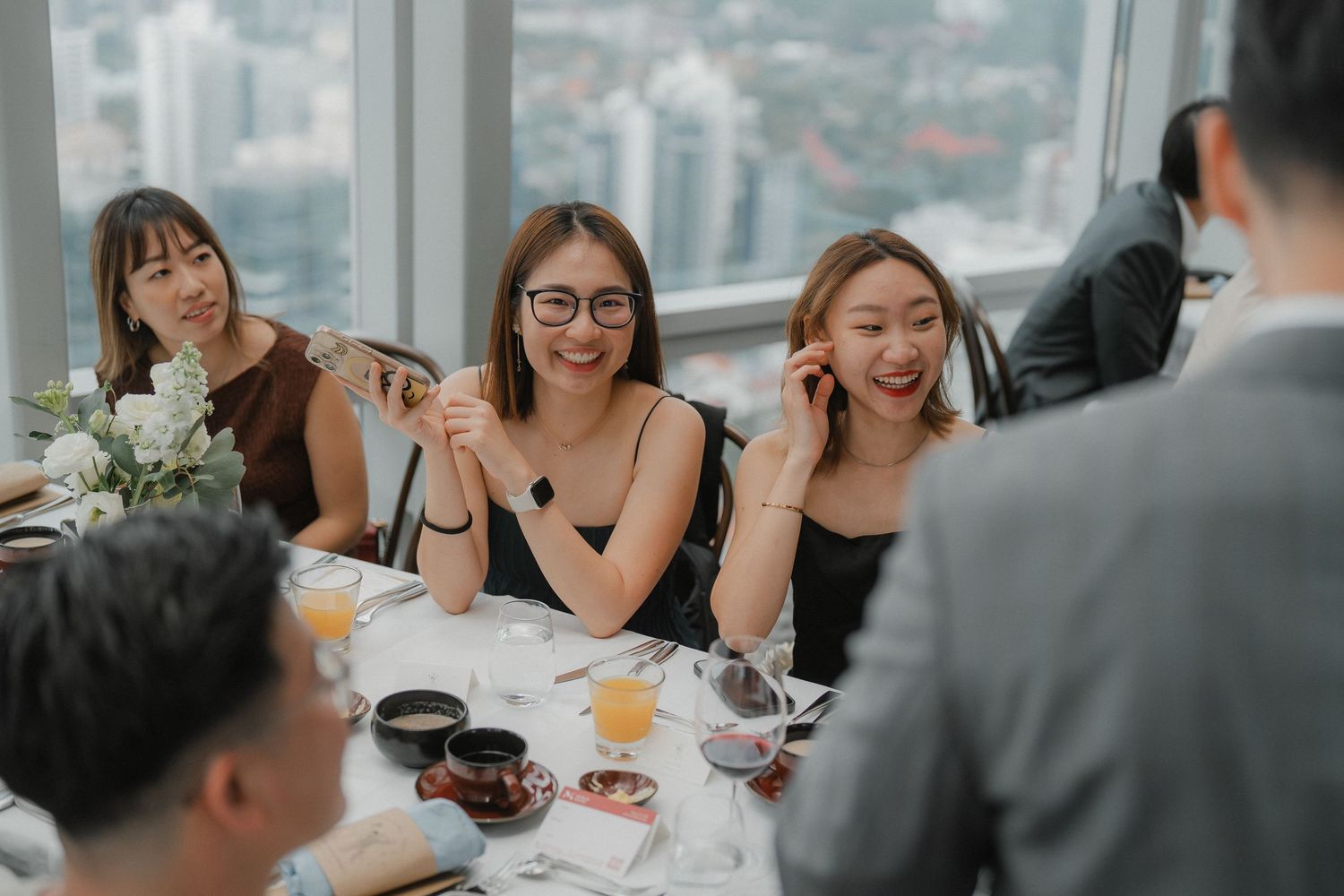 A group enjoying drinks and conversation at an elegant dining table with a city view.