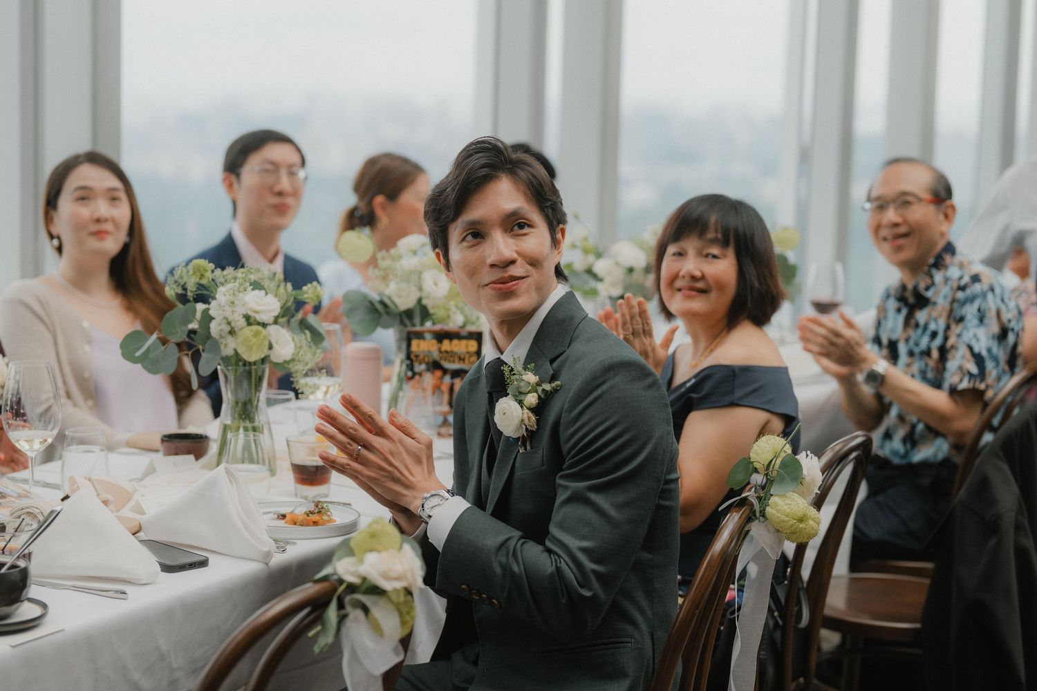Formal event attendees socialize and dine at elegantly set tables near floor-to-ceiling windows.