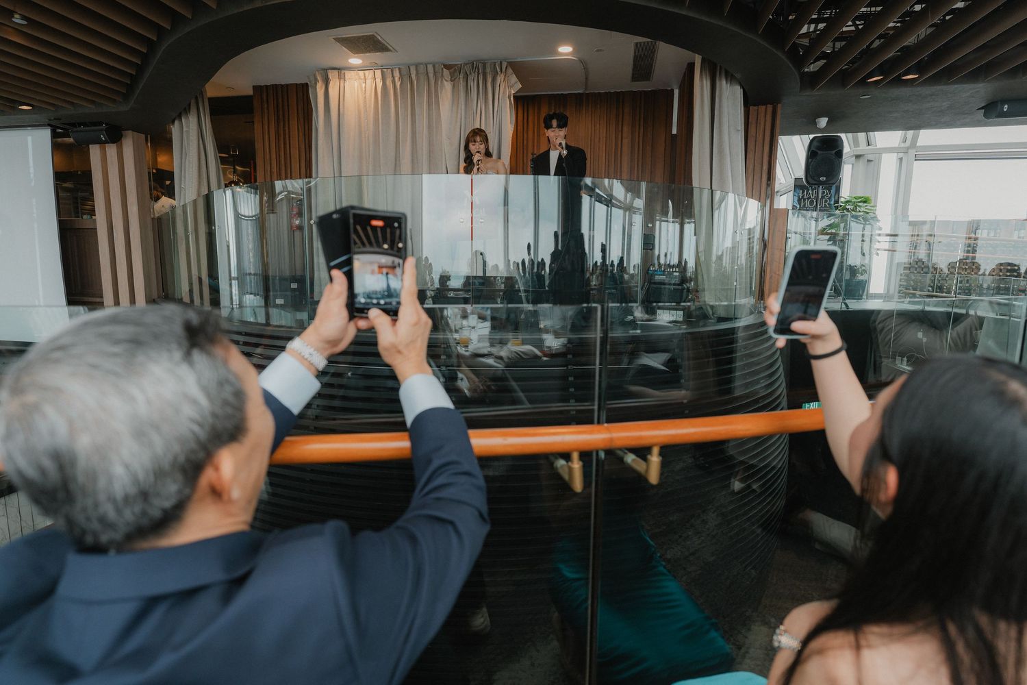 People taking photos with smartphones at an event through glass windows.