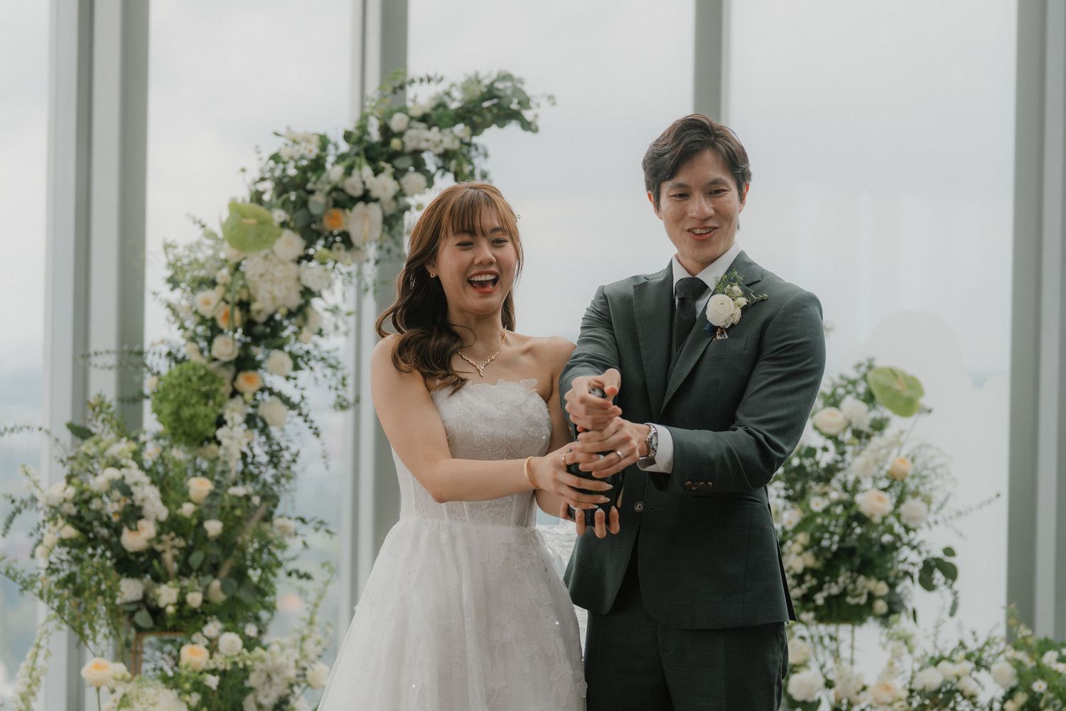 Intimate indoor wedding ceremony with floral arch and city views through glass windows.