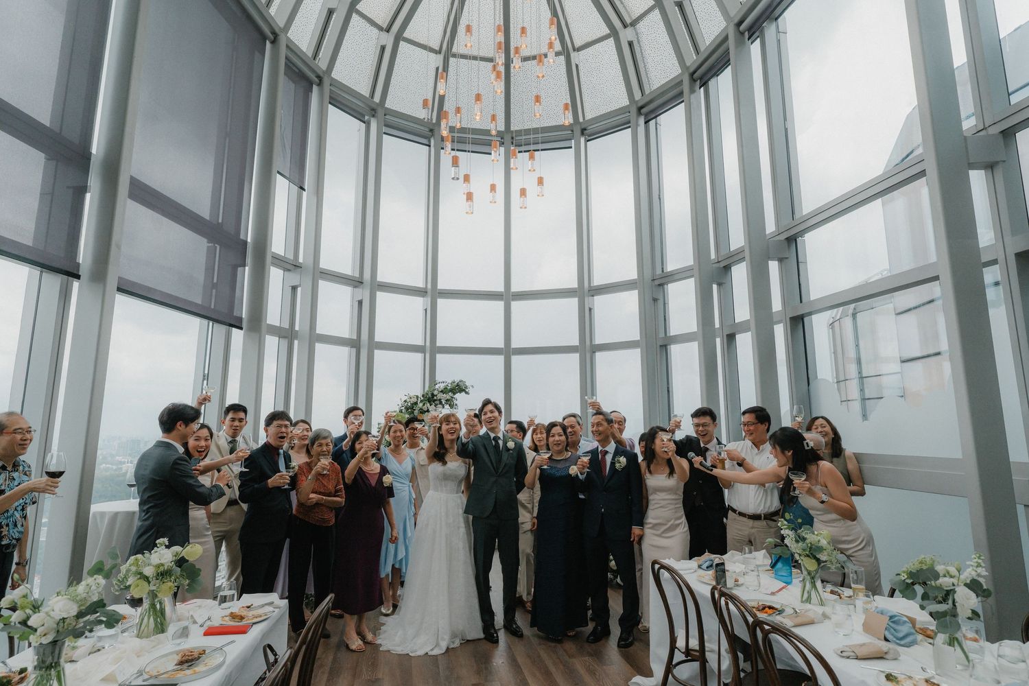 Wedding celebration in a glass dome venue with elegant table settings and city skyline views.