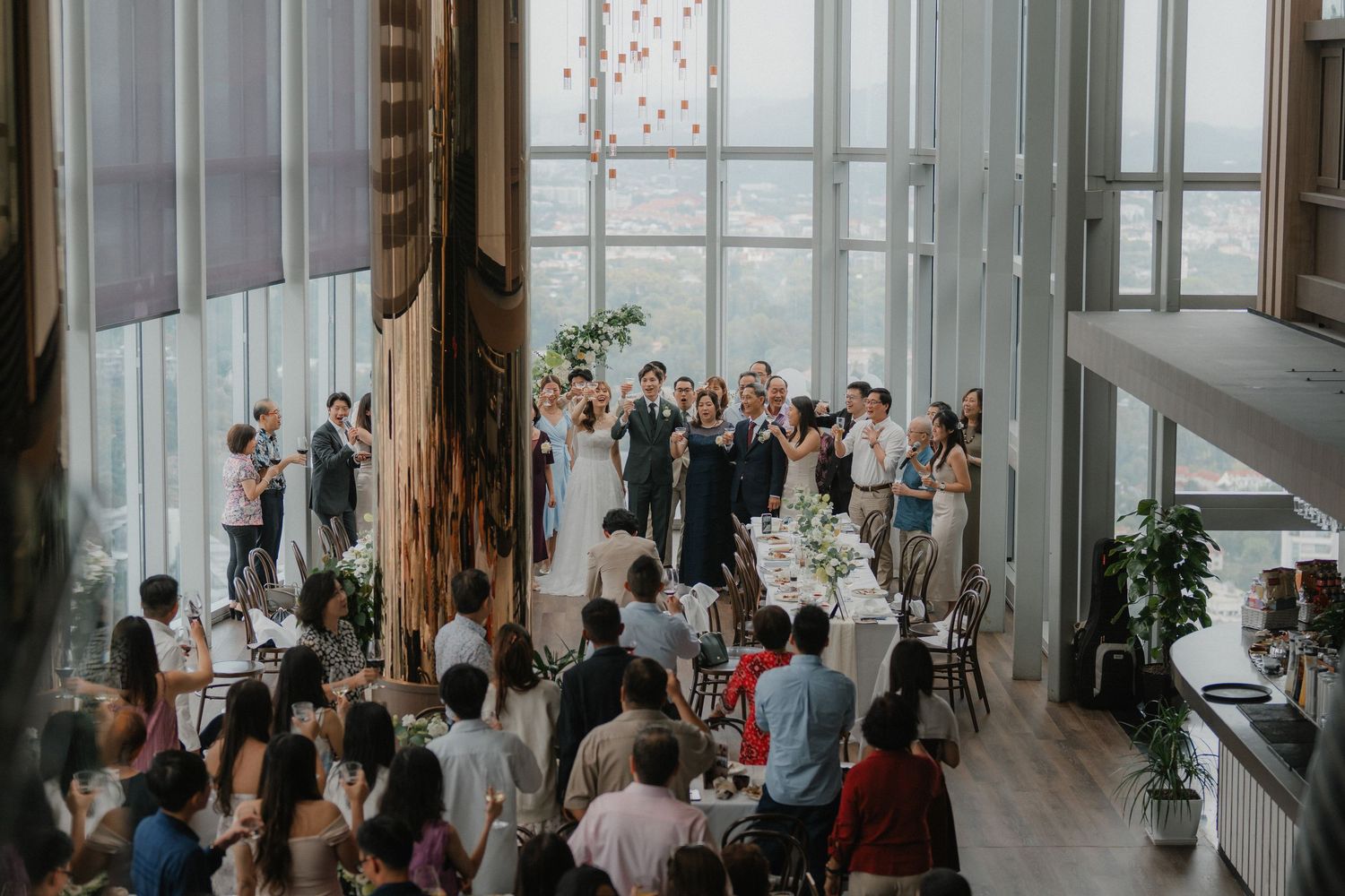 High angle view of wedding reception with guests mingling in modern venue with floor-to-ceiling windows.