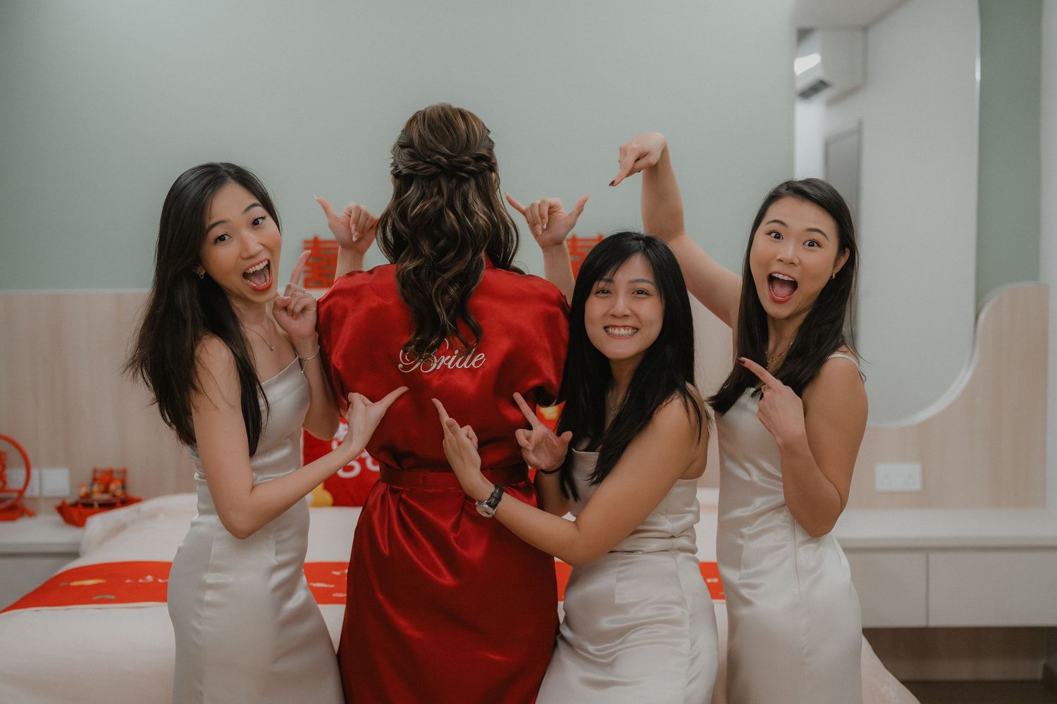 Wedding party celebrating in a room decorated with red accents as bridesmaids in ivory dresses dance together.