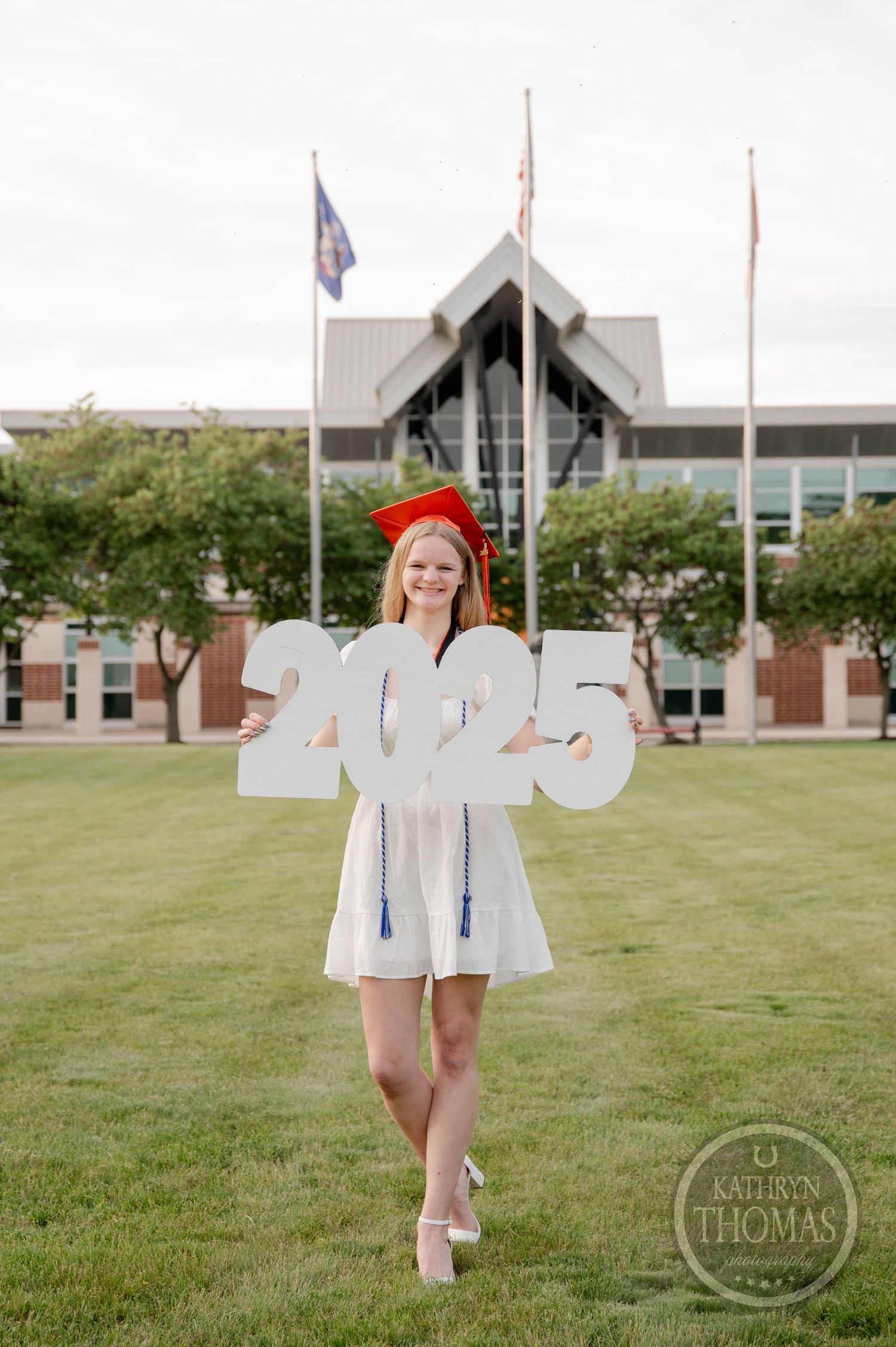 Graduate holds up individual letters outside on a grassy field with a building in the background.