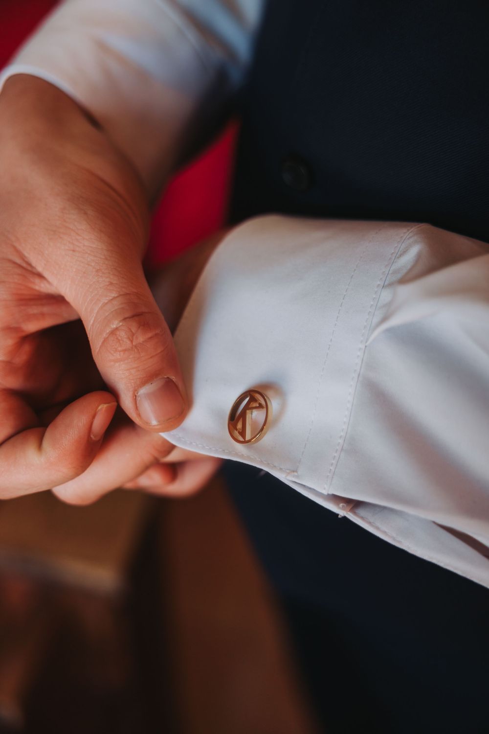 Hands fastening a gold cufflink on a crisp white dress shirt sleeve in closeup detail.