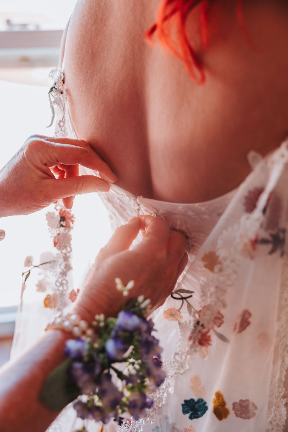 Close-up shot of delicate lace wedding dress details with purple wildflowers and floral embroidery.