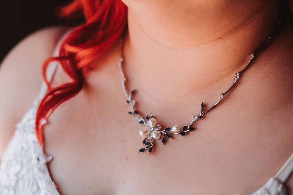Close-up of delicate silver floral necklace adorning neckline with red hair and white lace dress visible in frame.
