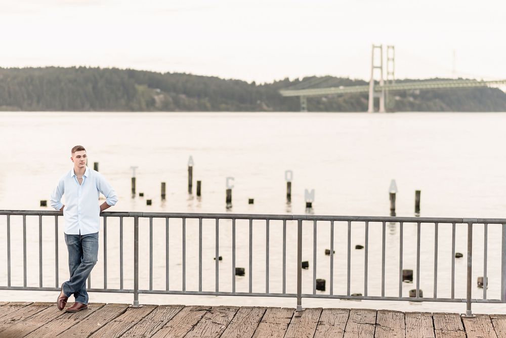 A serene pier extends into a calm blue bay with mountains and a bridge visible in the distance.