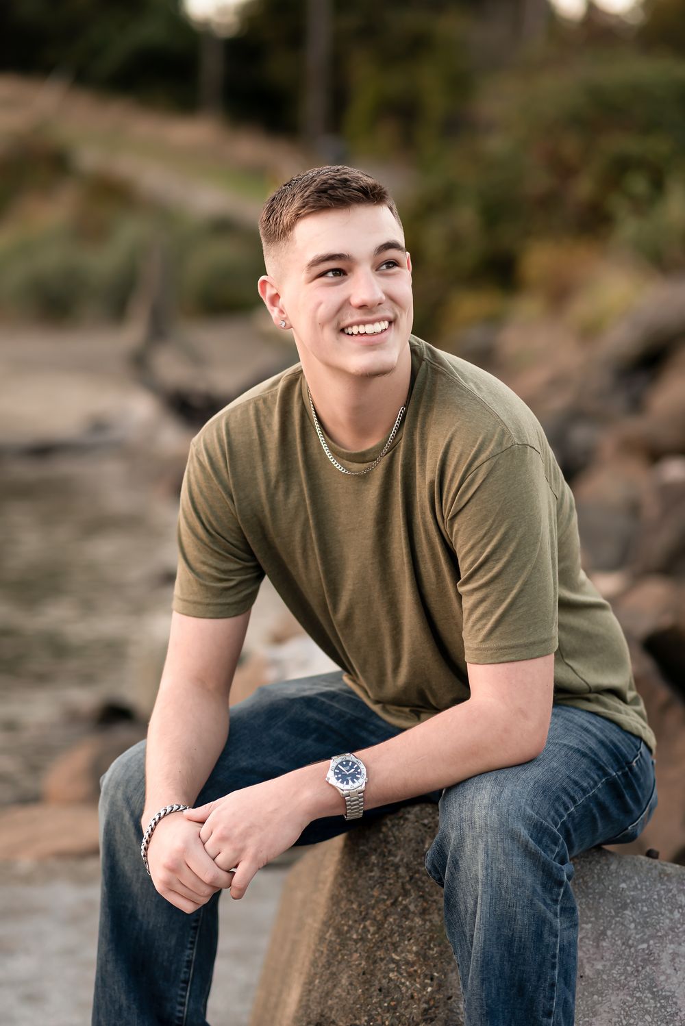 Someone wearing an olive t-shirt and jeans sits casually on a rocky shoreline during golden hour.