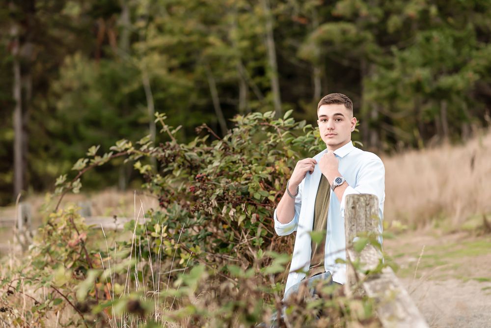 Person wearing a light blue top and vest stands in autumn field with dried grass and scattered trees in the background.