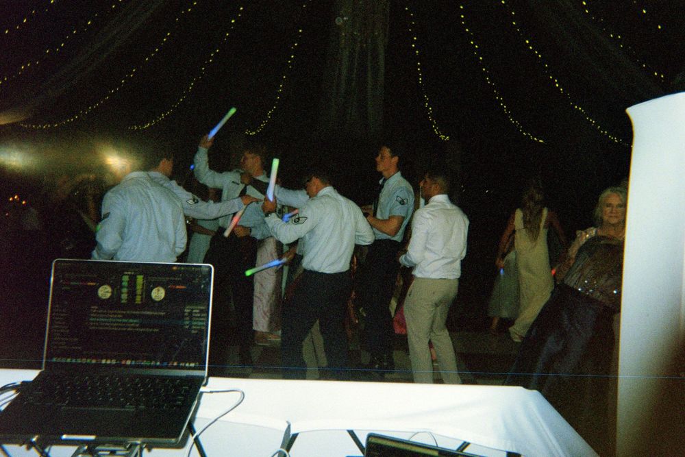 People dancing and enjoying themselves at a dimly lit party or nightclub event with DJ equipment visible.